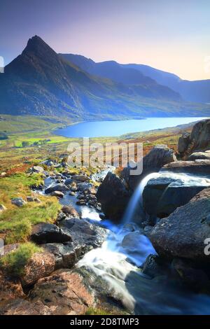 Kleiner Wasserfall mit Tryfan und Lyl Ogwen im Hintergrund an einem sonnigen Tag, Snowdonia National Park, Nordwales, Großbritannien. Stockfoto