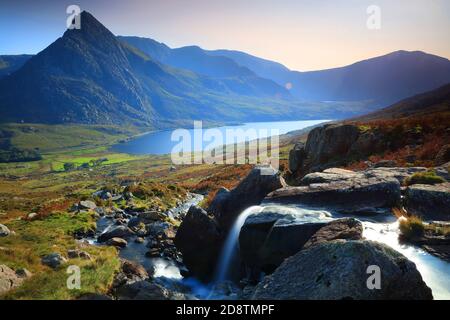 Kleiner Wasserfall mit Tryfan und Lyl Ogwen im Hintergrund an einem sonnigen Tag, Snowdonia National Park, Nordwales, Großbritannien. Stockfoto