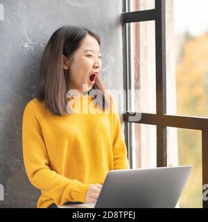 Asiatische Frau gähnend aufgrund überarbeiten und anstrengend. Junge Dame im leuchtend gelben Pullover Stockfoto