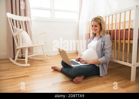 Attraktive junge schwangere Frau mit Laptop Stockfoto