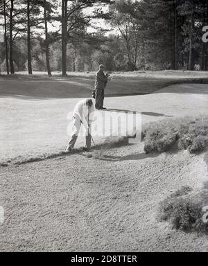 1960s, historisch, ein männlicher Golfer spielt aus einem Fairway oder Bunker, mit Caddy stehend Ebene mit ihm, trägt seine Golfschläger, England, Großbritannien. Stockfoto