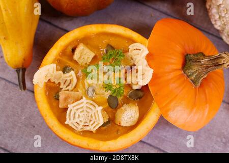 Kürbis halloween Suppe. Vegetarische Kürbiskarottensuppe in einem hohlen Kürbis mit Sahne, Kürbiskernen, Petersilie und Croutons. Herbst, Danksagung Stockfoto