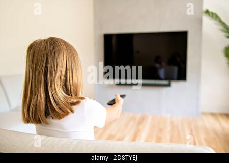 Rückansicht Bild von niedlichen kleinen blonden Haaren Mädchen auf dem Sofa sitzen und Fernsehen. Stockfoto