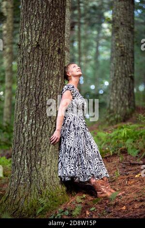 Fröhliche Frau, die sich im Wald gegen einen Baum lehnt und in Staunen aufschaut - Brevard, North Carolina, USA Stockfoto