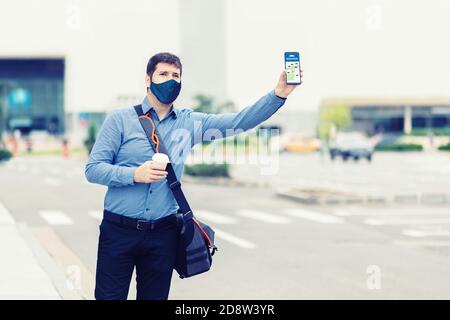 Mann Passagier mit Schutzmaske Gesicht mit mobilen Taxi-App Wartende Kabine oder Mitfahrgelegenheit mit der Hand nach oben Stockfoto