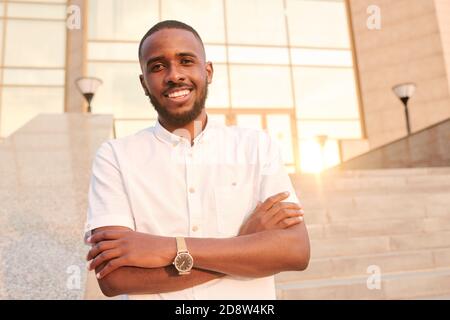 Afrikanischer Geschäftsmann mit toothy Lächeln stehend mit gekreuzten Armen Nach Brust Stockfoto