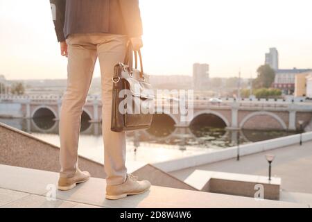 Rückansicht des jungen eleganten Geschäftsmannes mit Handtasche stehend auf Oben auf der Treppe Stockfoto