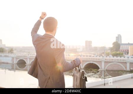 Rückansicht des jungen gewinnenden Geschäftsmannes mit Lederhandtasche zum Ausdruck bringen Triumph Stockfoto