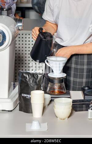 Weibliche Barista-Hände bereiten den Kaffee zu, indem sie kochendes Wasser aus einem schwarzen Wasserkocher in einen weißen Trichter einer Glaskolbe gießen. Stockfoto