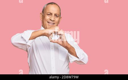 Schöner älterer Mann trägt elegante weiße Hemd lächelnd in Liebe tun Herz Symbol Form mit Händen. Romantisches Konzept. Stockfoto