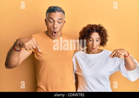 Schönes Paar mittleren Alters zusammen tragen lässige Kleidung nach unten mit Fingern zeigt Werbung, überrascht Gesicht und offenen Mund Stockfoto