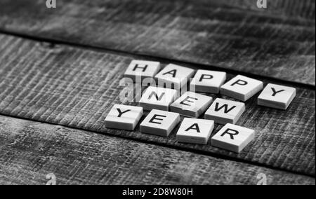 Fröhliches Neujahr Schriftzug. Briefe auf Holzpostkarten auf dunklem Holzhintergrund. Schwarzweiß-Fotografie. Stockfoto