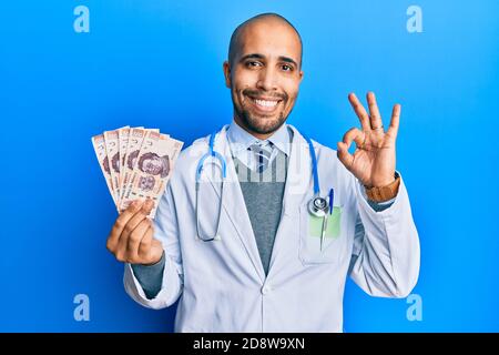 Hispanic erwachsenen Arzt Mann trägt medizinische Uniform hält 500 mexikanische Pesos tun ok Zeichen mit Fingern, lächelnd freundlich gestikulieren ausgezeichnetes Symbol Stockfoto