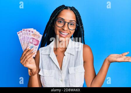 Schöne hispanische Frau hält 50 mexikanische Pesos Banknoten feiern Leistung Mit glücklichen Lächeln und Sieger Ausdruck mit erhobener Hand Stockfoto