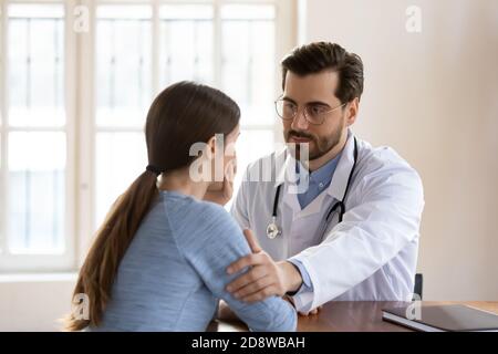 Der behandelnde Arzt berührt die Schulter des gestressten Patienten und zeigt Unterstützung Stockfoto