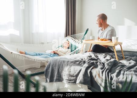 Junges Paar zu Hause sitzen und gute Zeit haben, während Frühstück im Bett. Glückliche Familie in der Wohnung etwas zu reden und verbringen Zeit zusammen Stockfoto