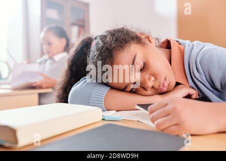 Erschöpft oder gelangweilt Schulmädchen in Casualwear halten den Kopf auf dem Schreibtisch Beim Nickerchen Stockfoto