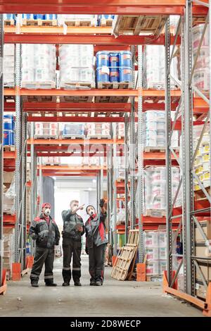 Gruppe von Lagerarbeitern in Handschuhen, Atemschutzgeräten und Arbeitskleidung diskutieren Waren Stockfoto