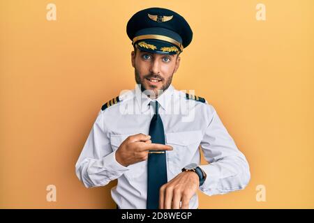 Schöner hispanischer Mann trägt Flugzeug-Pilot Uniform in Eile zeigt, um Zeit, Ungeduld, aufgeregt und wütend auf Deadline-Verzögerung zu beobachten Stockfoto