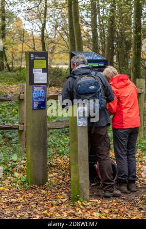 Eine Frau und ein Mann tragen Outdoor-Kleidung mit einem Parkuhr oder Pay-Maschine in einem Waldparkplatz in norfolk. Stockfoto