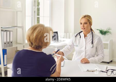 Reife Frau diskutieren ihre Behandlung mit jungen Arzt in modernen Krankenhausbüro Stockfoto