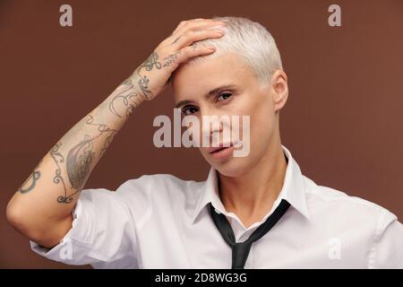 Manlike reife Geschäftsfrau mit Tätowierungen ganz über ihren Arm halten Hand auf Kopf Stockfoto