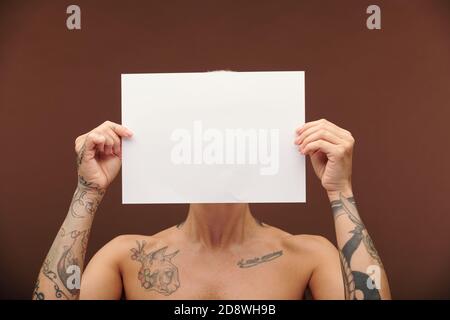 Junge männliche Frau mit Tätowierungen auf Armen, Brust und Hals mit leerem Papier Stockfoto