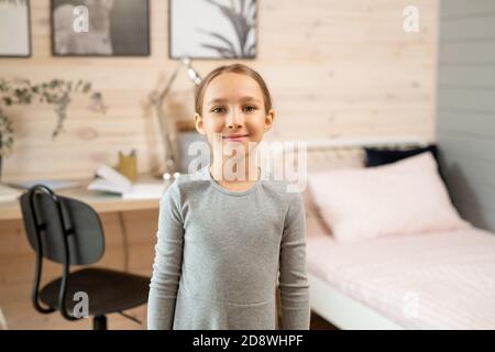 Zeitgenössische Schülerin in grauem Kleid vor der Kamera stehen Gegen das Zimmer Stockfoto