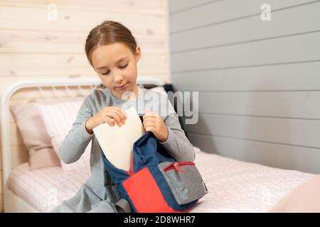 Ernst Schulmädchen in grauem Kleid Putting Buch in Rucksack vor Schule Stockfoto