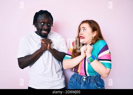 Interracial paar tragen legere Kleidung lachen nervös und aufgeregt mit Hände am Kinn, die zur Seite schauen Stockfoto
