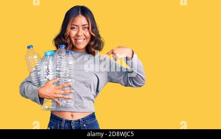 Junge schöne gemischte Rasse Frau hält Recycling-Plastikflaschen zeigen Finger zu einem selbst lächelnd glücklich und stolz Stockfoto