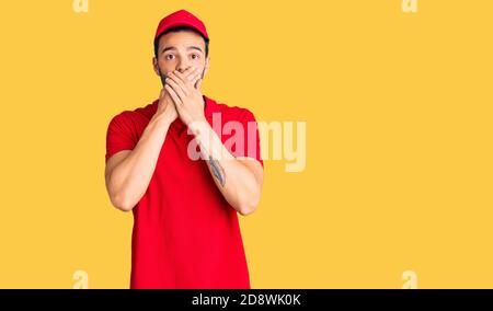 Junge gut aussehende hispanischen Mann trägt Lieferung Kurier Uniform schockiert Abdeckung Mund mit Händen für Fehler. Secret Konzept. Stockfoto