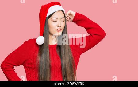 Junge chinesische Frau trägt weihnachtsmütze, die sich zurückzieht, müde und entspannt, schläfrig und gähnend für den frühen Morgen Stockfoto