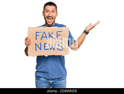 Hübscher Mann mit Tattoos, die gefälschte Nachrichten halten, die den Sieg feiern Mit glücklichen Lächeln und Sieger Ausdruck mit erhobenen Händen Stockfoto