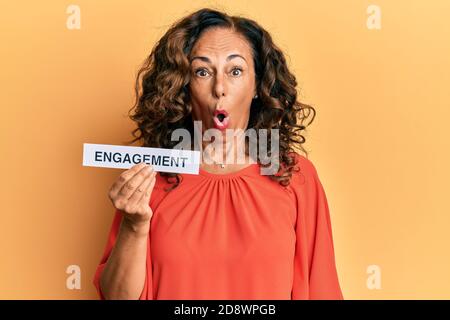 Mittelalter hispanische Frau hält Engagement Wortpapier verängstigt und erstaunt mit offenem Mund für Überraschung, Unglauben Gesicht Stockfoto