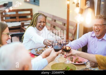 Glückliche ältere multirassische Freunde jubeln mit Wein und essen Grill - Fokus auf afrikanische Frau Stockfoto