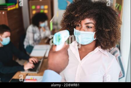 Mann mit Infrarot-Stirnthermometer zur Überprüfung der Körpertemperatur von Arbeiter - Fokus auf das rechte Auge der Frau Stockfoto