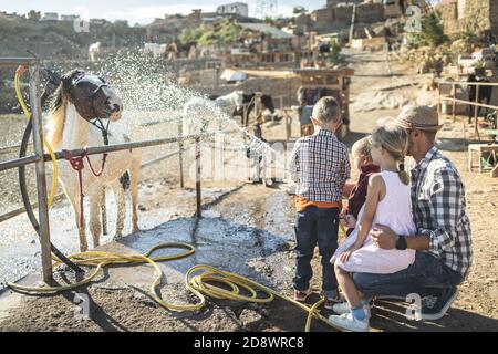 Glückliche Familie mit Vater und Kindern waschen ihr Pferd im Freien Auf Ranch Farm - Fokus auf linken Kopf Kind Stockfoto