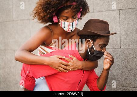 Glückliches junges Paar mit Gesichtsmaske in der Stadt - Afrikaner und Huckepack Stockfoto