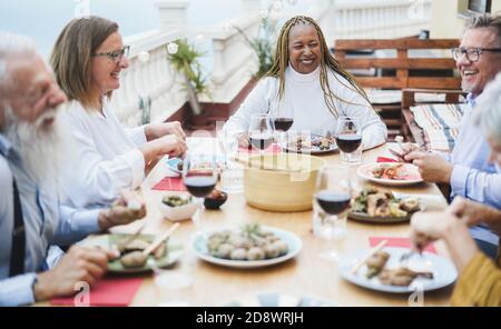 Ältere, multirassische Menschen, die beim Abendessen auf der Terrasse Spaß haben - glücklich Friends Eating at sunday Meal - Focus on african Woman Stockfoto