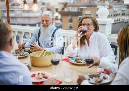 Ältere, multirassische Menschen, die beim Abendessen auf der Terrasse Spaß haben - glücklich Friends Eating at sunday Meal - Fokus auf Hipster Mann Gesicht Stockfoto