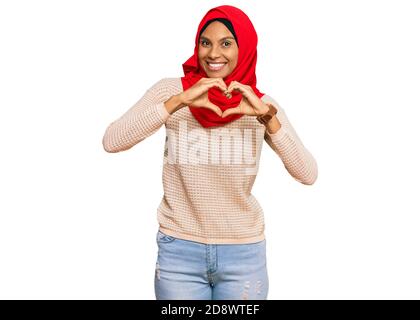 Junge afroamerikanische Frau trägt traditionelle islamische Hijab Schal lächelnd in der Liebe tun Herz Symbol Form mit Händen. Romantisches Konzept. Stockfoto