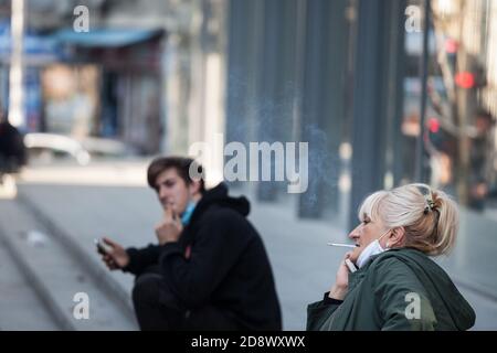 BELGRAD, SERBIEN - 10. OKTOBER 2020: Zwei Angestellte, eine Frau und ein Mann mit einer Atemmaske, die eine Pause machen und während der Zeit eine Zigarette rauchen Stockfoto