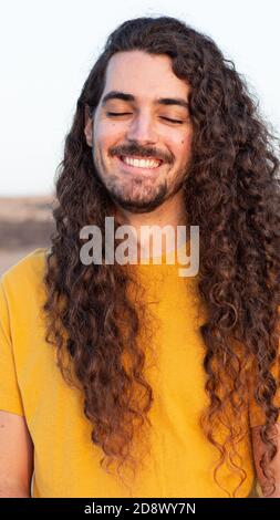 Vertikale Aufnahme eines lächelnden jungen Mannes mit langen Locken Haare Stockfoto