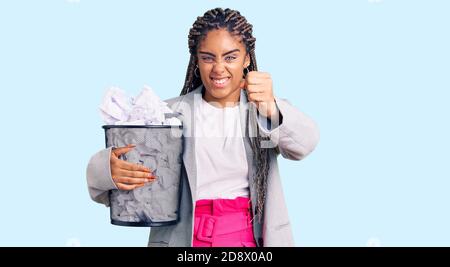 Junge afroamerikanische Frau mit Zöpfen, die Papierbehälter voller zerknitterter Papiere hielten, verärgert und frustriert, vor Wut schreiend, verrückt nach Wut schreiend Stockfoto