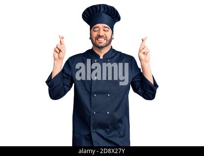 Junge hispanic Mann trägt Herd Uniform gestikulierenden Finger überquert lächelnd mit Hoffnung und Augen geschlossen. Glück und abergläubischen Konzept. Stockfoto