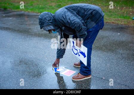 Brooklyn, NY - 1. November 2020. Die Wähler in Brooklyns Midwood-Nachbarschaft standen in einem leichten Regen an einem Wahllokal im Brooklyn College in einer Reihe, um ihre Stimmzettel am letzten Tag der vorzeitigen Wahl bei den Präsidentschaftswahlen 2020 in New York abzustimmen. Nachdem die letzten Wähler im Viereck waren, nahm ein Umfragearbeiter Richtungsschilder auf. Stockfoto