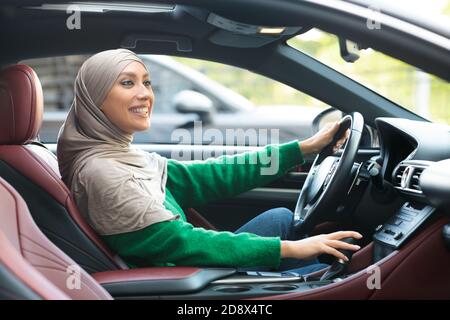 Lächelnde muslimische Frau fährt ihr neues Auto in der Stadt Stockfoto