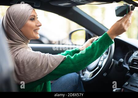 Junge muslimische Frau, die alleine fährt und Rückspiegel anpasst Stockfoto