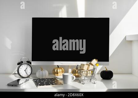 Leerer Bildschirm-Desktop-Computer in modernem minimalem Büroraum mit Herbstdekorationen. Papierkartons in einem Trolley auf dem Schreibtisch. Online-Shopping-Konzept Stockfoto